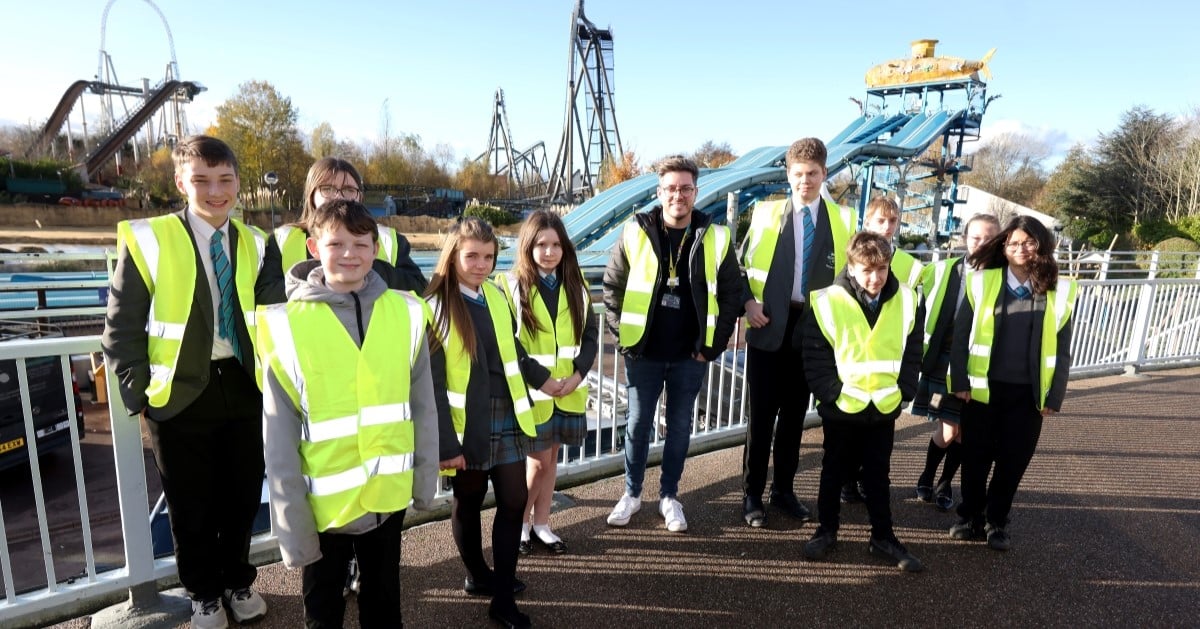 Young people and adults wearing high vis jackets pose in front of a theme park attraction.