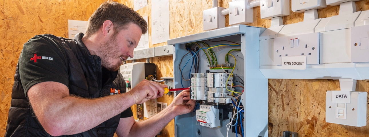 An electrician with a screwdriver fixing a fuse box
