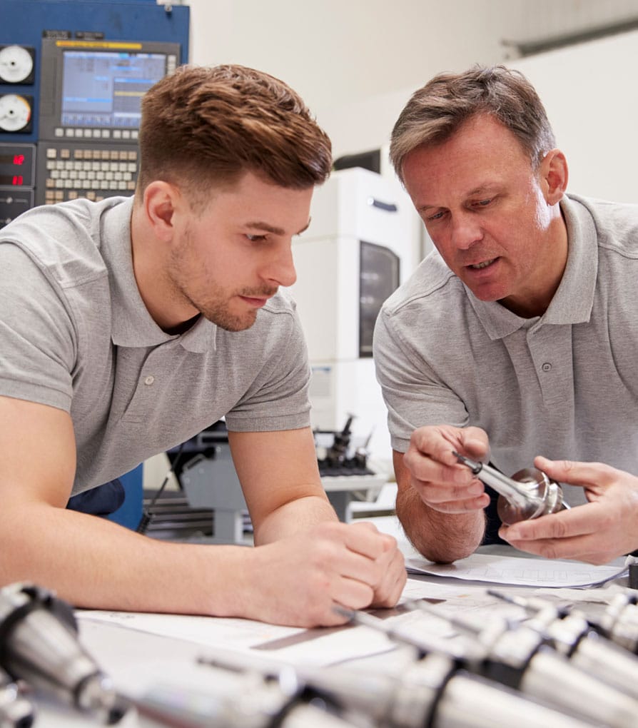 Plumbing apprentice being shown a part by another man