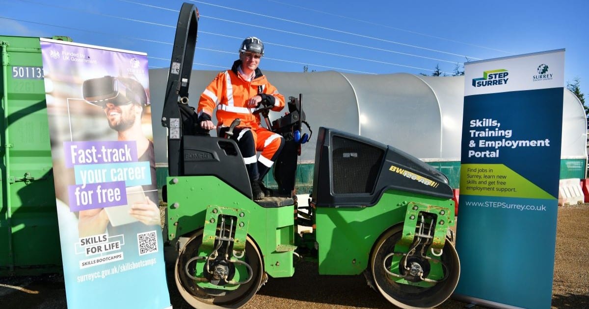 A man in orange hi-vis sits on a roller in a construction site. Either side are banners for Skills Bootcamps and STEP Surrey.