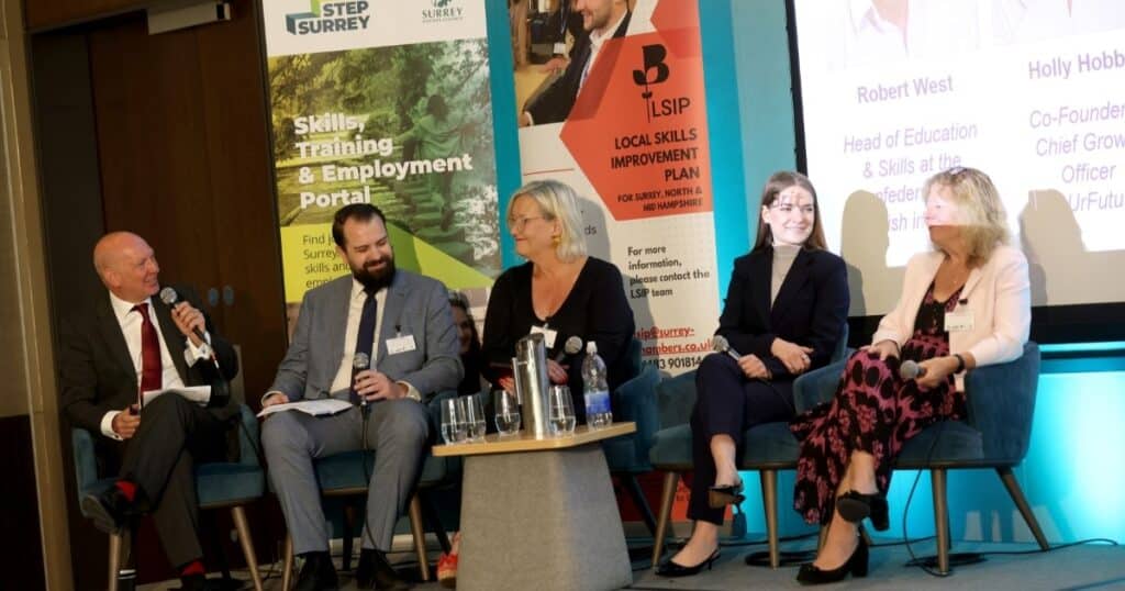 Five people sit on a conference stage. Behind them are two banners for STEP Surrey and Surrey Chambers of Commerce