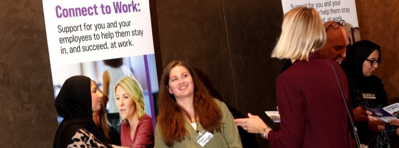 Three women stand talking at a skills event stood in front of a Connect to Work banner
