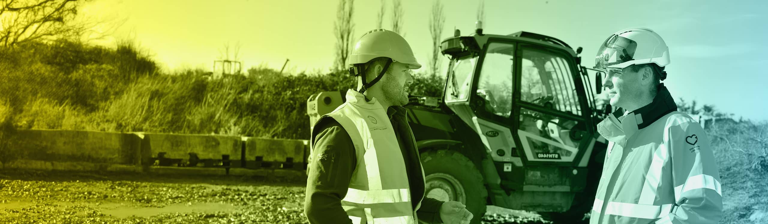 Two men in hard hats and high vis jackets facing each other next to a vehicle