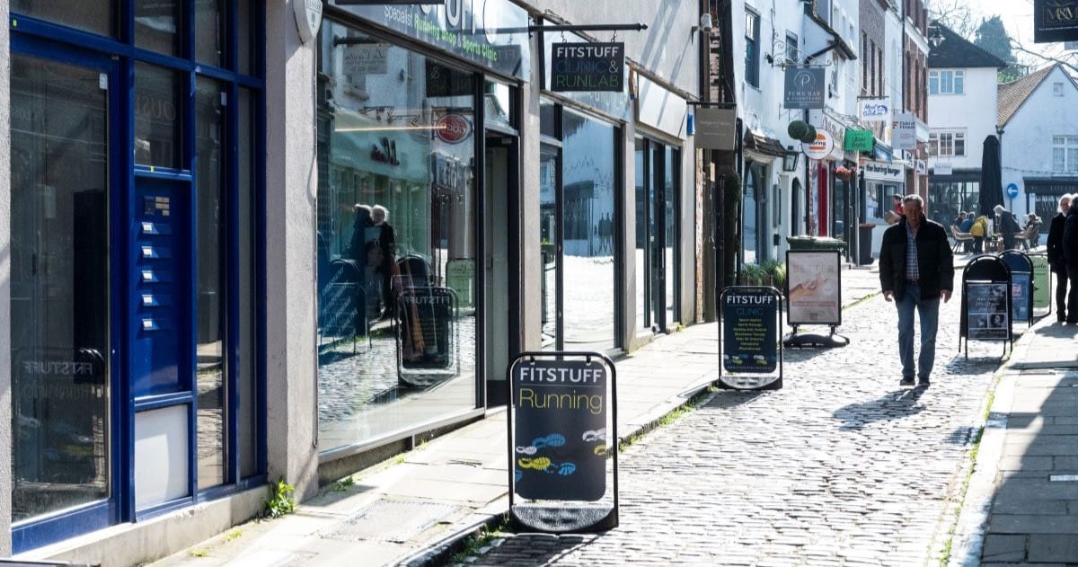 Image of a high street with shoppers walking down a cobbled street past along a number of shops.