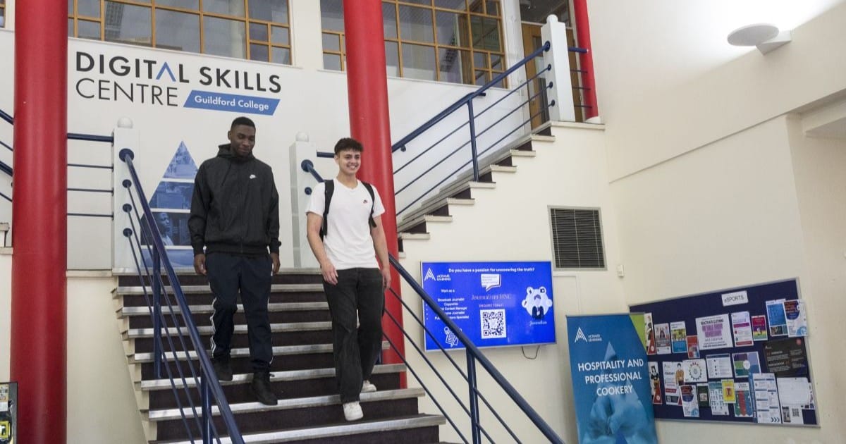 Two young adults in casual clothes walk down stairs in a college building. Behind them is a sign for Digital Skills Centre